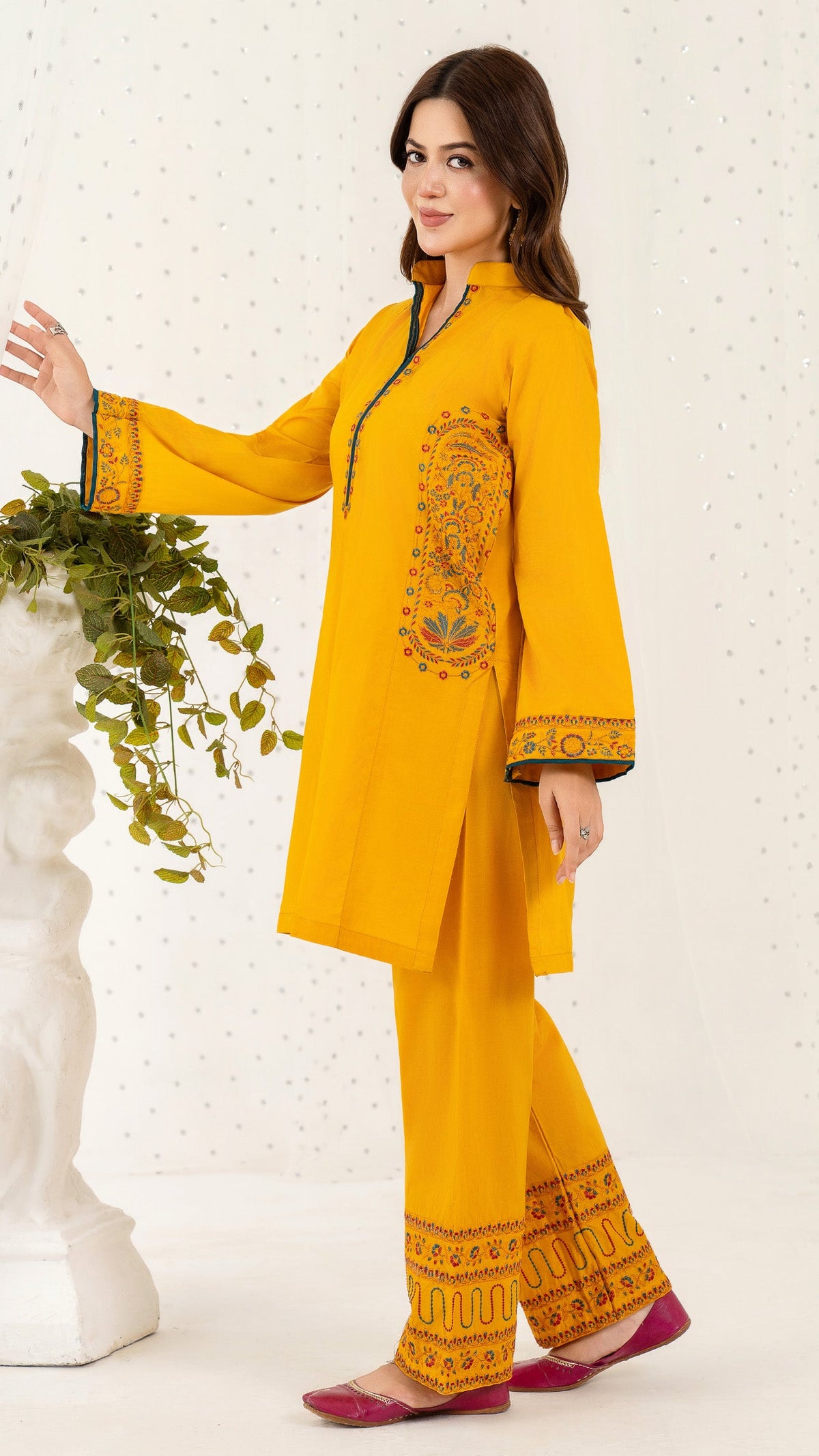 Woman wearing a yellow embroidered outfit standing against a white background